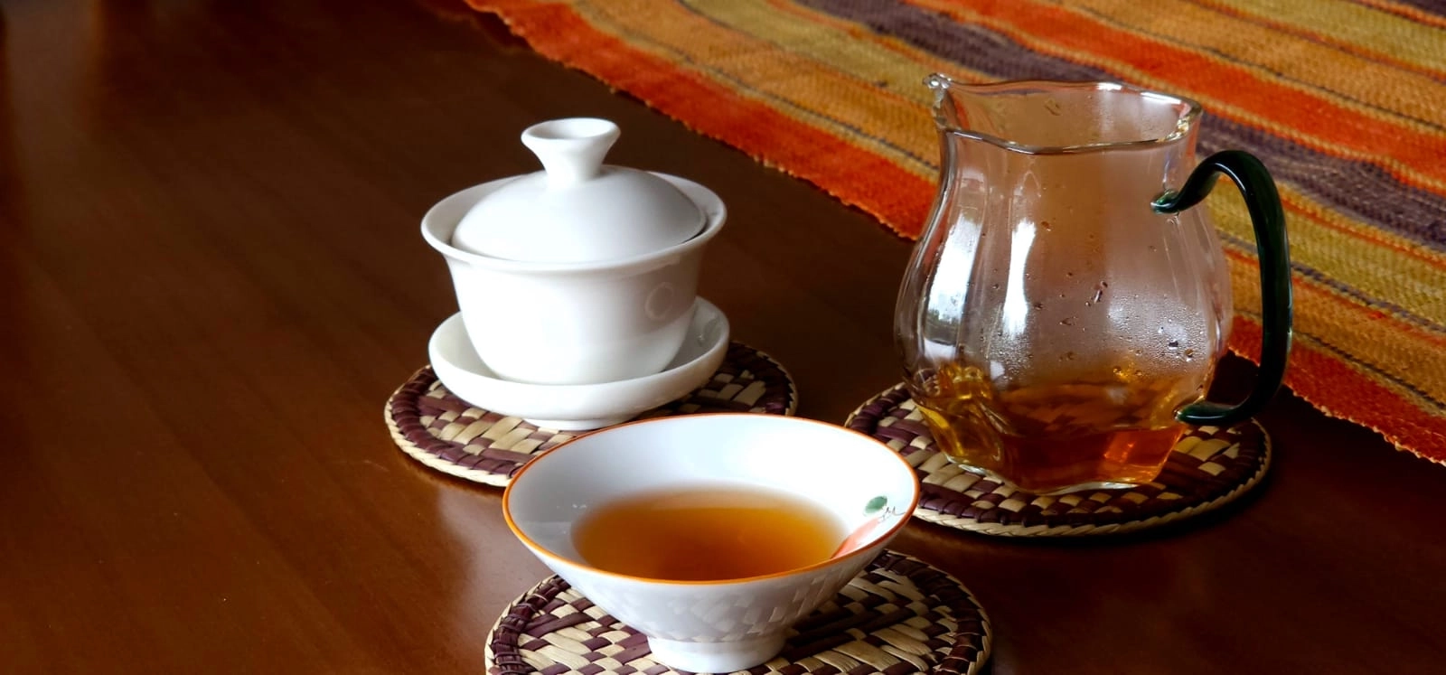 Chá servido em gaiwan, xícara e jarra de vidro sobre mesa de madeira